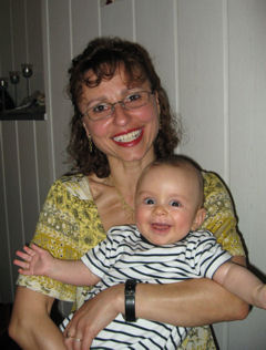 Hebamme h&auml;lt lachendes Baby auf dem Arm